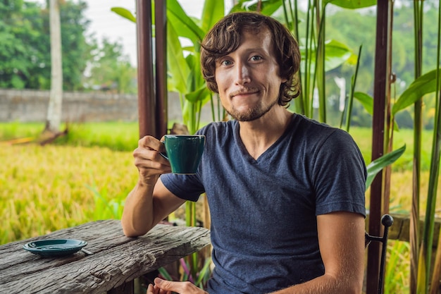 Man with a cup of coffee on the cafe veranda near the rice terraces on Bali, Indonesia.