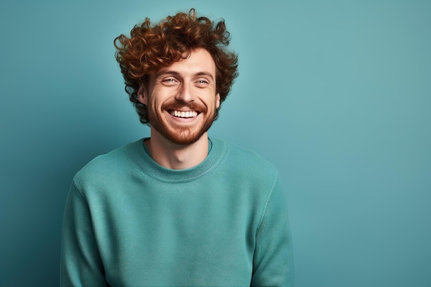 A man with curly ginger hair is smiling and wearing a blue sweater