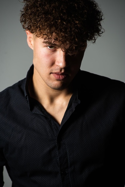 A man with curly hair wears a black shirt with a white collar.