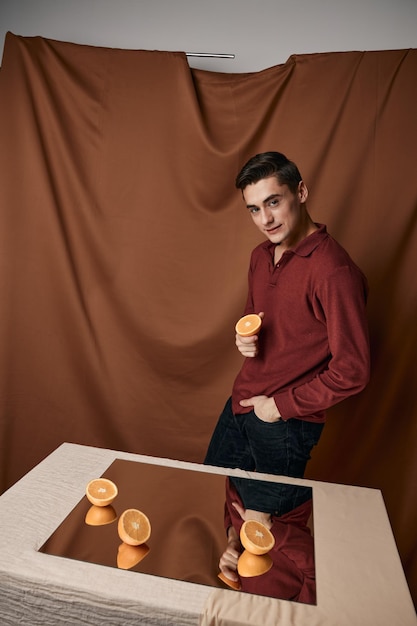 Man with cut oranges on the table and fabric background reflected in the mirror