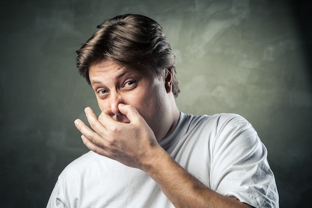 Man with disgusted expression closing his nostrils with his fingers