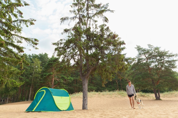 Man with Dog by tent under a tree on a sandy beach