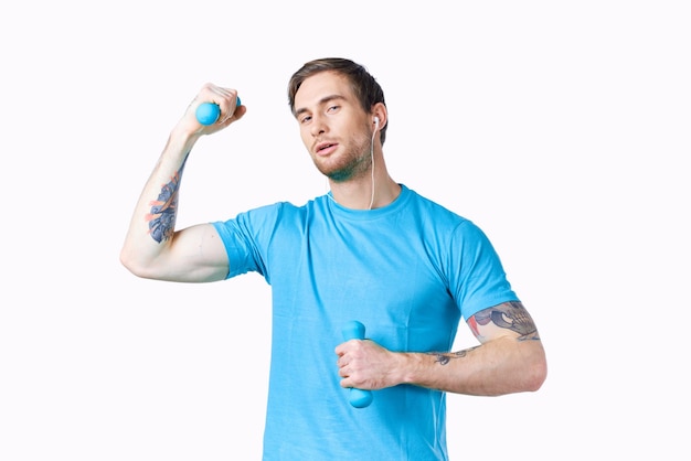 Man with dumbbells in his hands and in a blue tshirt on a light background cropped view of a fitness model