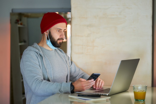 A man with a face mask working on his laptop