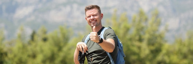 Man with finnish sticks for nordic walking holds thumbs up on mountain sports lifestyle and