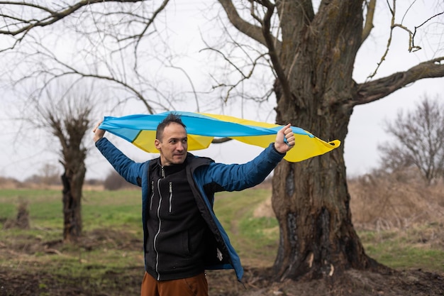 man with the flag of Ukraine near the burnt tree.