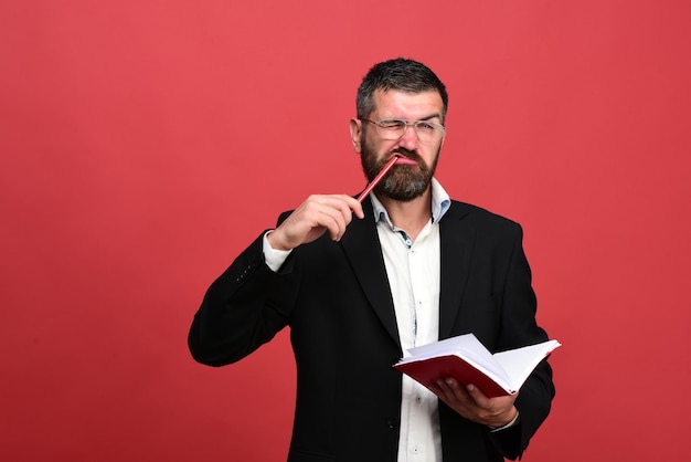 Man with funny face holds book and pencil in mouth on red background