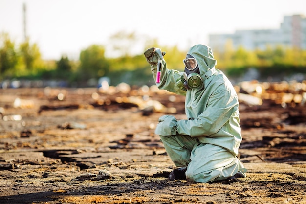 Man with gas mask and green military clothes explores barrels after chemical disaster