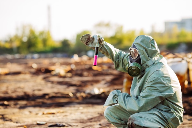 Man with gas mask and green military clothes explores barrels after chemical disaster