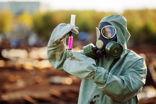 Man with gas mask and green military clothes explores barrels after chemical disaster