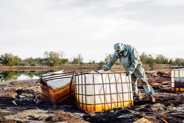 Man with gas mask and green military clothes explores barrels after chemical disaster