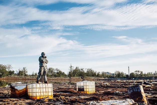 Man with gas mask and green military clothes explores barrels after chemical disaster