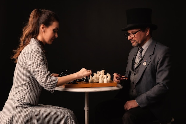 A man with a girl plays chess and smokes a pipe on a dark background