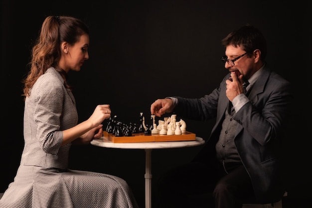 A man with a girl plays chess and smokes a pipe on a dark background