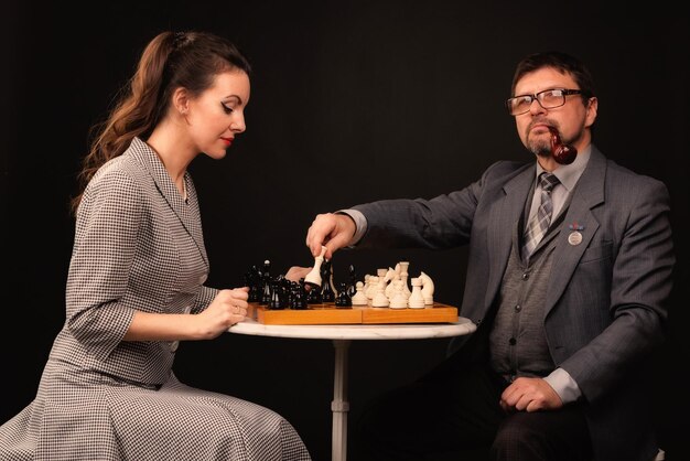 A man with a girl plays chess and smokes a pipe on a dark background