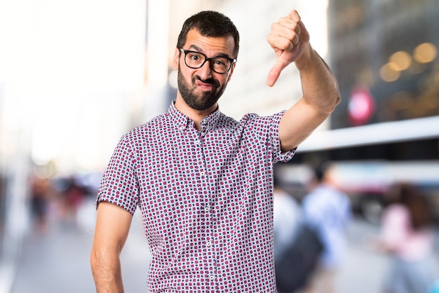 Man with glasses doing bad signal on unfocused background