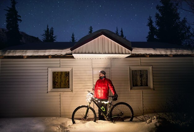 Man with glowing bicycle near house in forest