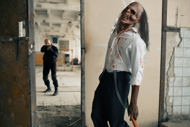 Man with gun fights with undead zombie, nightmare in abandoned factory. Horror in city, creepy crawlies, doomsday apocalypse, bloody evil monster