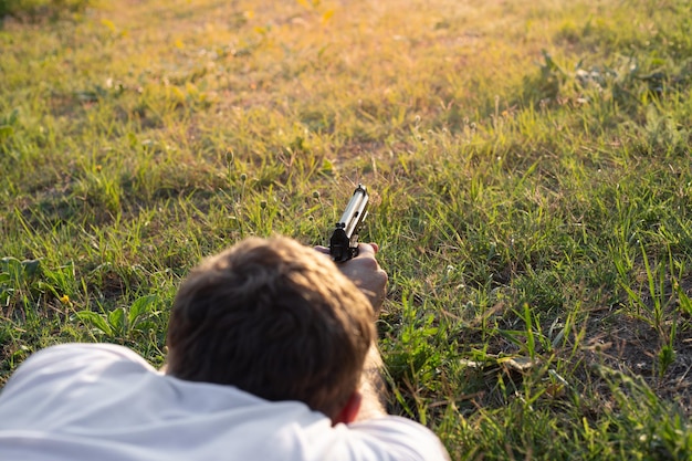 A man with a gun lying on the grass shoots copy space