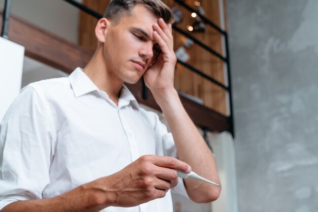 Man with a headache holds a digital thermometer