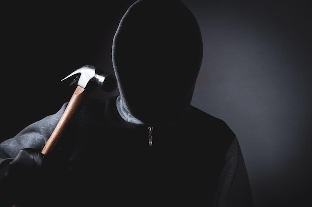 Man with a hood and a mask on his face threatens with a hammer