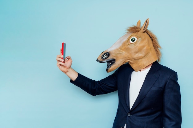 man with horse mask taking a selfiBusinessman with horse mask taking a selfie