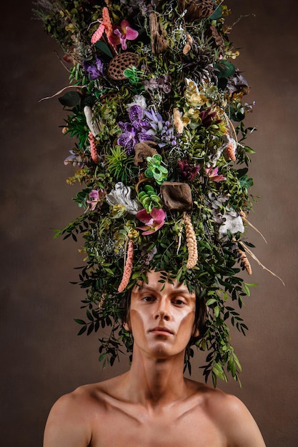 A man with a huge elongated headdress made of living diverse vegetation and flowers A child of nature a fabulous creature Art object