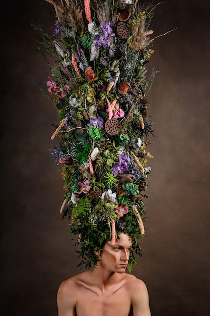 A man with a huge elongated headdress made of living diverse vegetation and flowers A child of nature a fabulous creature Art object