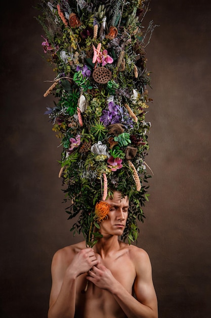 A man with a huge elongated headdress made of living diverse vegetation and flowers A child of nature a fabulous creature Art object