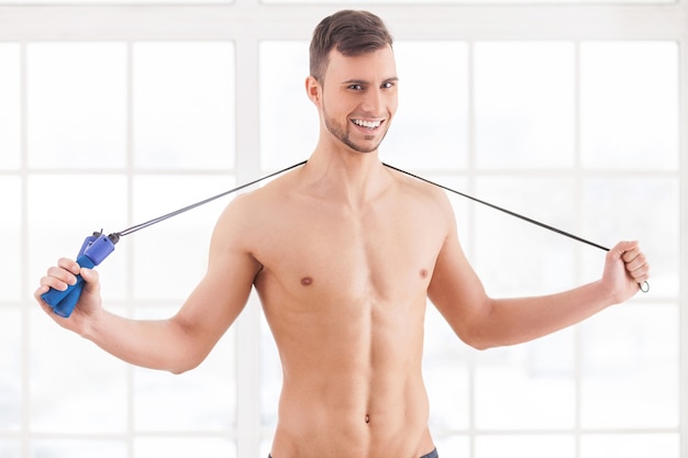 Man with jumping rope. Young muscular man holding a skipping rope on his shoulders and smiling at camera