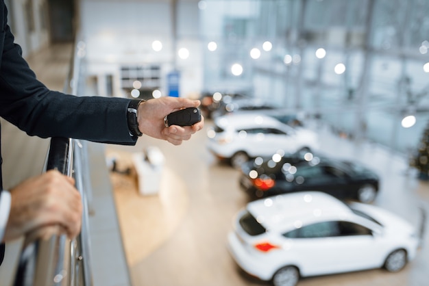 Man with keys from his new transport in car dealership. Customer in new vehicle showroom, male person buying automobile, auto dealer business