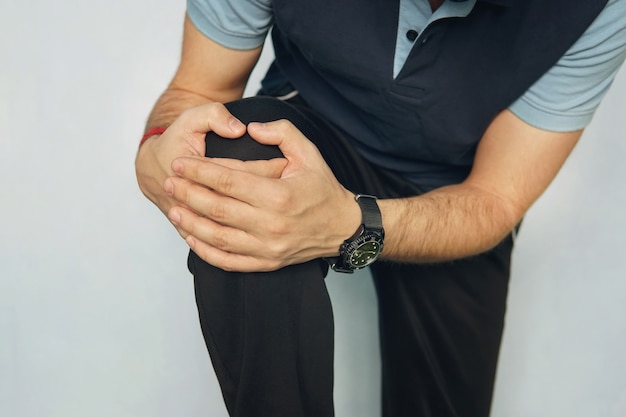 Man with knee pain on color background. young man is holding his hands over his sick knee on a blue background. athlete in a tracksuit with a pain in the thigh in training