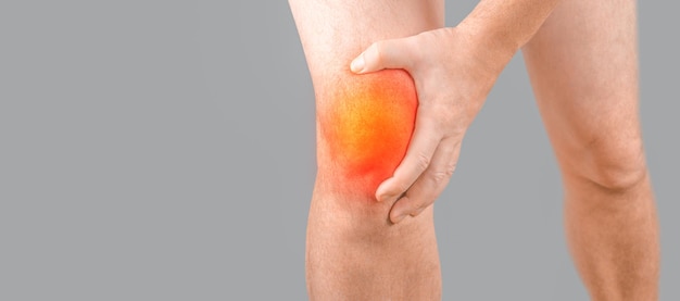 Man with knee pain on gray background Man leg knee with red dot Knee injury sprain arthritis or meniscus Man having problems in knee joint Closeup view copy space