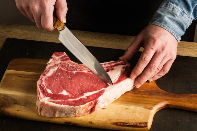 Man with a knife in his hand cutting a veal steak on a wooden kitchen board