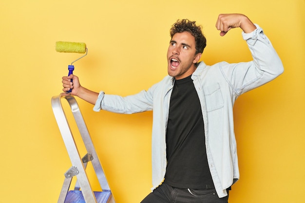 Photo man with ladder and paint roller on yellow raising fist after a victory winner concept