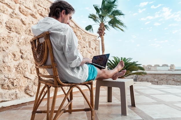 A man with a laptop is resting and working as a freelancer on the background of palm trees