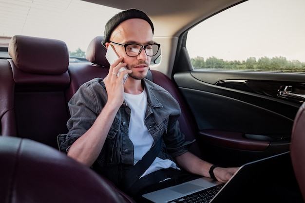 Man with laptop making phone call on a backseat of a car on trip to work.