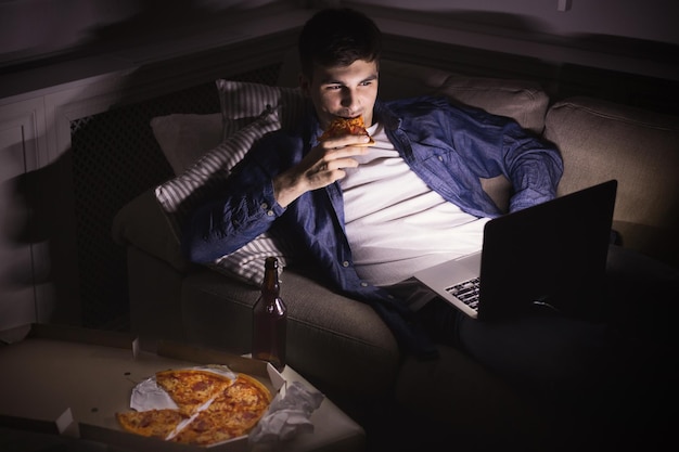 Man with laptop, pizza and beer at home in the evening. Watching movie or online football game, relaxing after workday