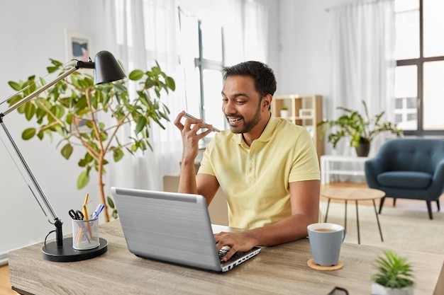 Photo man with laptop recording voice on phone at home