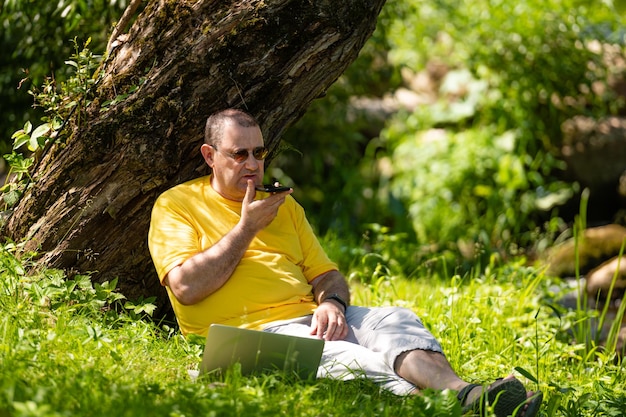 Man with laptop and smartphone working outside in the meadow by the river outdoor office concept