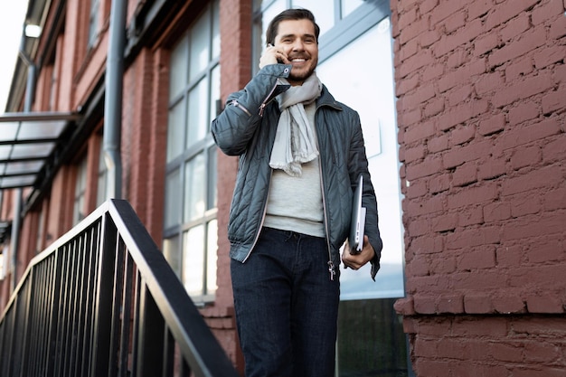 A man with a laptop talking on a mobile phone leaving the office building