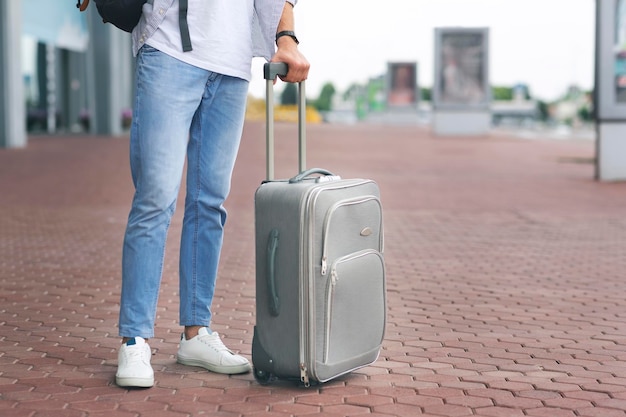 Man with luggage standing at airport parking waiting for taxi or bus