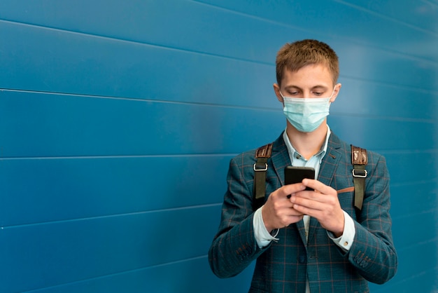 Man with medical mask and backpack using smartphone