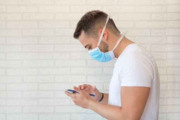 A man with a medical mask protecting against the virus or flu, in quarantine and communicating with his loved ones through his smartphone.