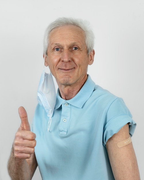 Man with medical mask showing thumbs up with bandage on arm after vaccine shot