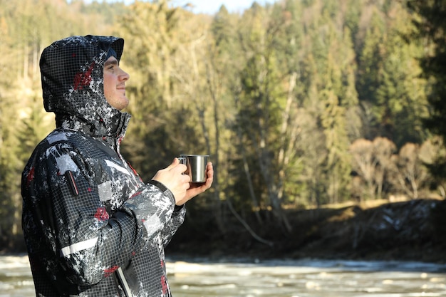 Man with metal cup stands near river