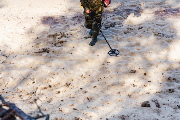 A man with a metal detector walks at the water's edge of a sandy beach