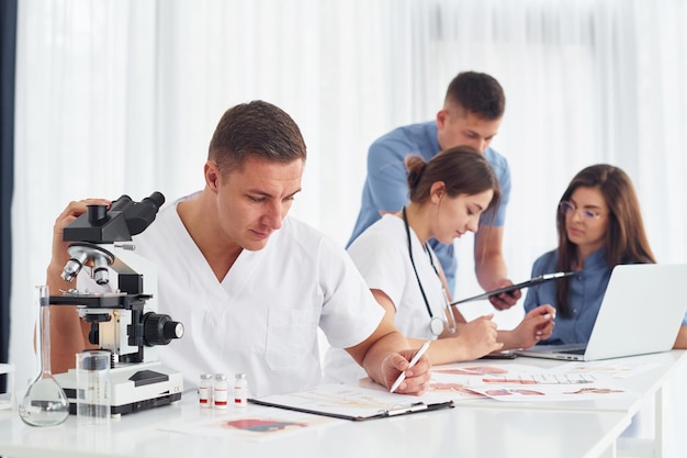 Photo man with microscope group of young doctors is working together in the modern office