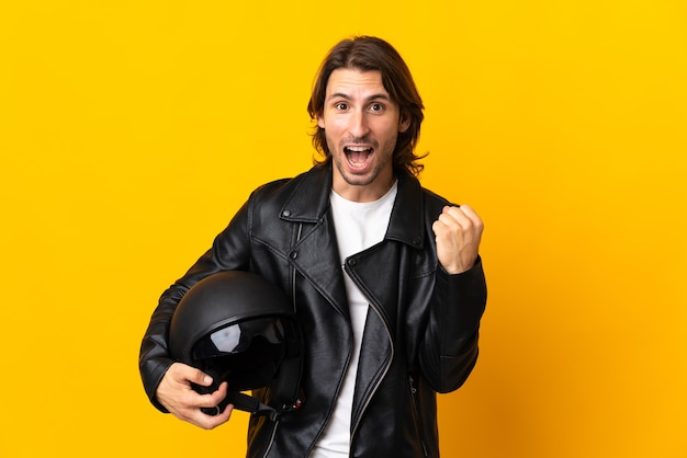 Man with a motorcycle helmet isolated on yellow background celebrating a victory in winner position