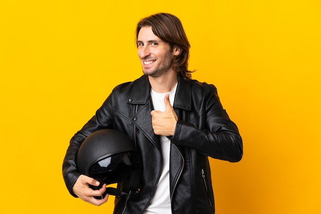 Man with a motorcycle helmet isolated on yellow background giving a thumbs up gesture